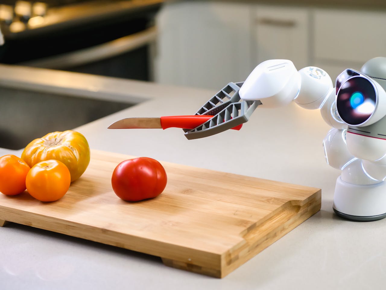 A futuristic robot assists in slicing a tomato in a modern kitchen setting.